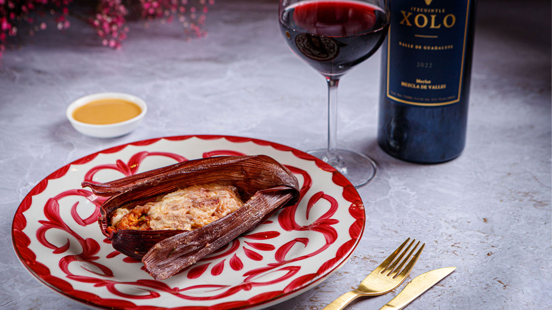 Tamal enjitomatado con quesillo y frijol blanco envuelto con hojas de totomoxtle morado. Se acompañó con Merlot de Xolo Vino, de notas de frutos secos y rojos maduros.